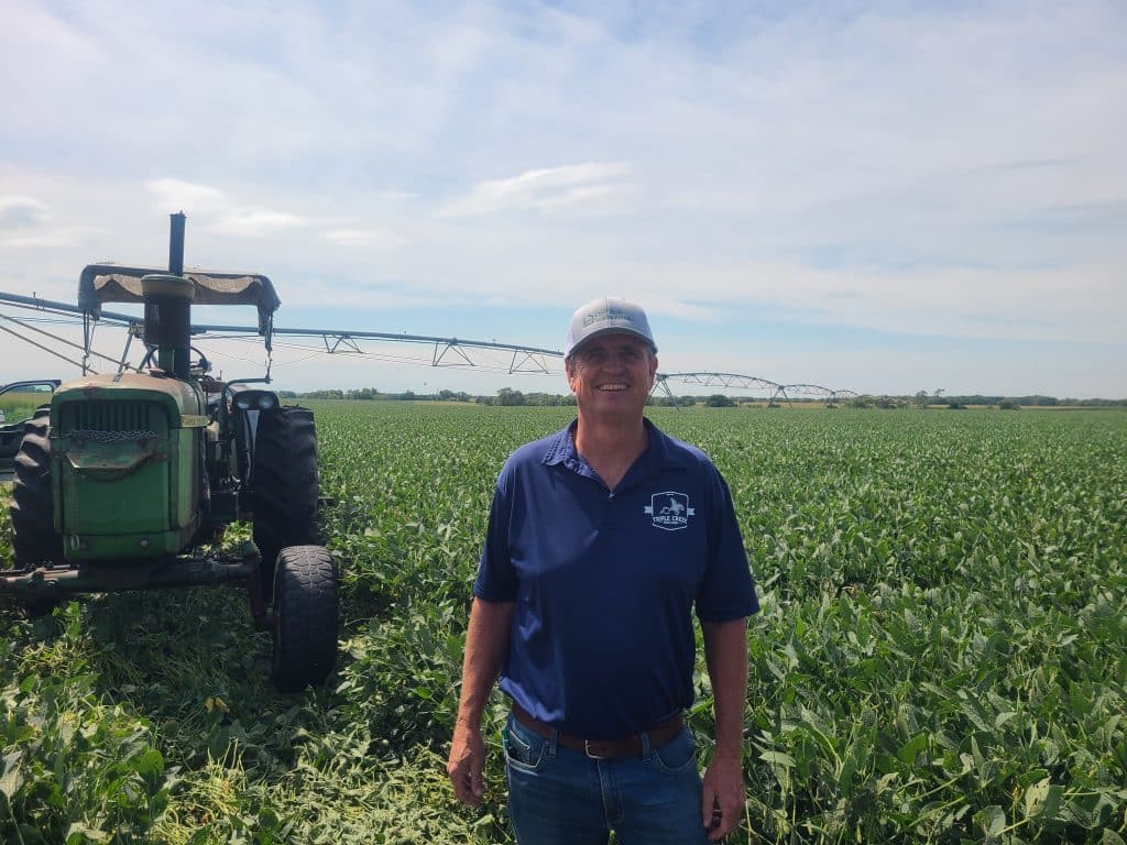 Vance McCoy smiling and standing in a field next to a tractor.